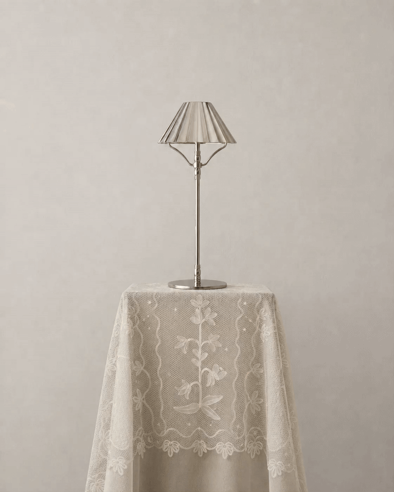 A silver cordless lamp set on a tablecloth presentation is switched on and off
